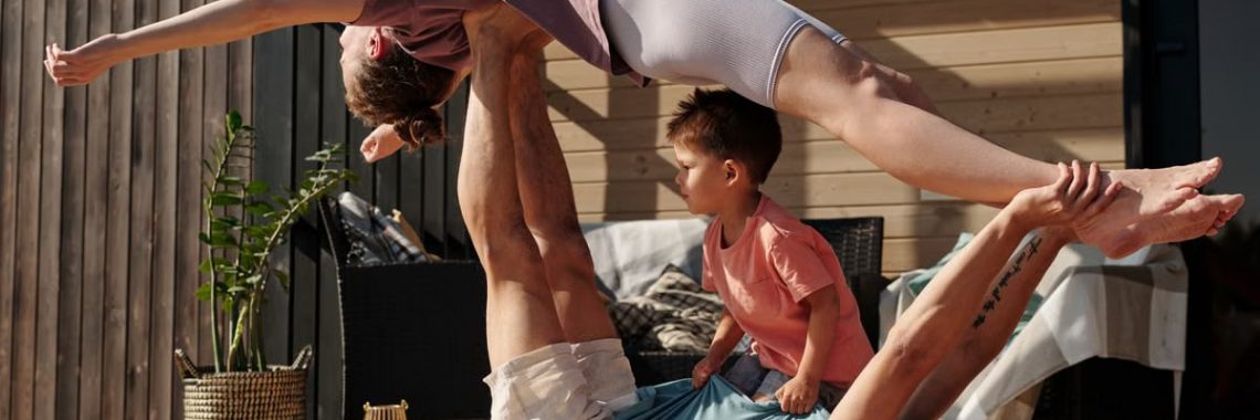 Father and kids doing yoga outdoors on a patio, balancing poses together.