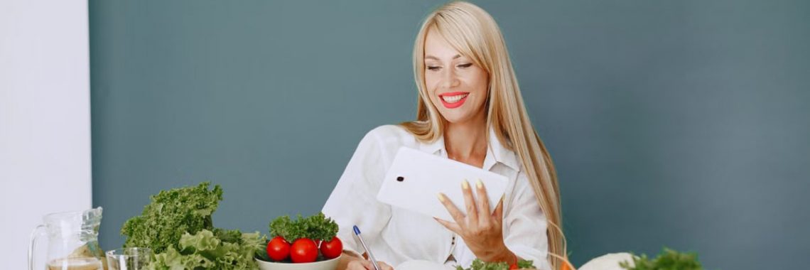 Woman using a tablet surrounded by fresh vegetables at a table, showcasing healthy lifestyle and technology.