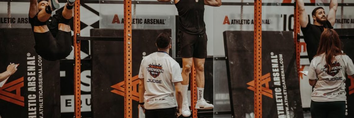 Athletes performing pull-ups in a CrossFit competition, judged by officials, showcasing strength and endurance.